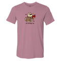 A heathered dusty rose short-sleeve t-shirt with a cartoon graphic of a dog wearing a trench coat and holding a red book, surrounded by autumn leaves, with the text 'all booked up' printed below.