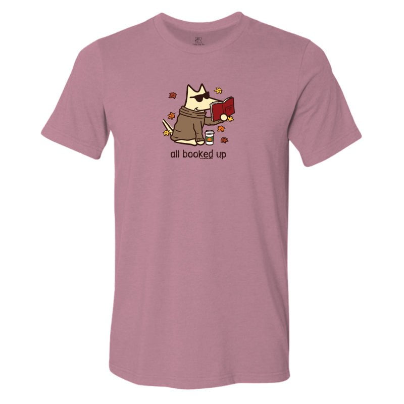 A heathered dusty rose short-sleeve t-shirt with a cartoon graphic of a dog wearing a trench coat and holding a red book, surrounded by autumn leaves, with the text 'all booked up' printed below.