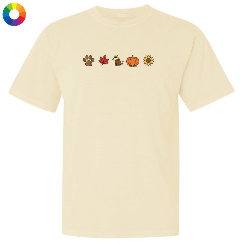 A cream-colored short-sleeve t-shirt with a horizontal row of small autumn-themed icons printed on the chest, including a paw print, maple leaf, dog, pumpkin, and sunflower. A circular multicolor color wheel icon is visible in the top-left corner.