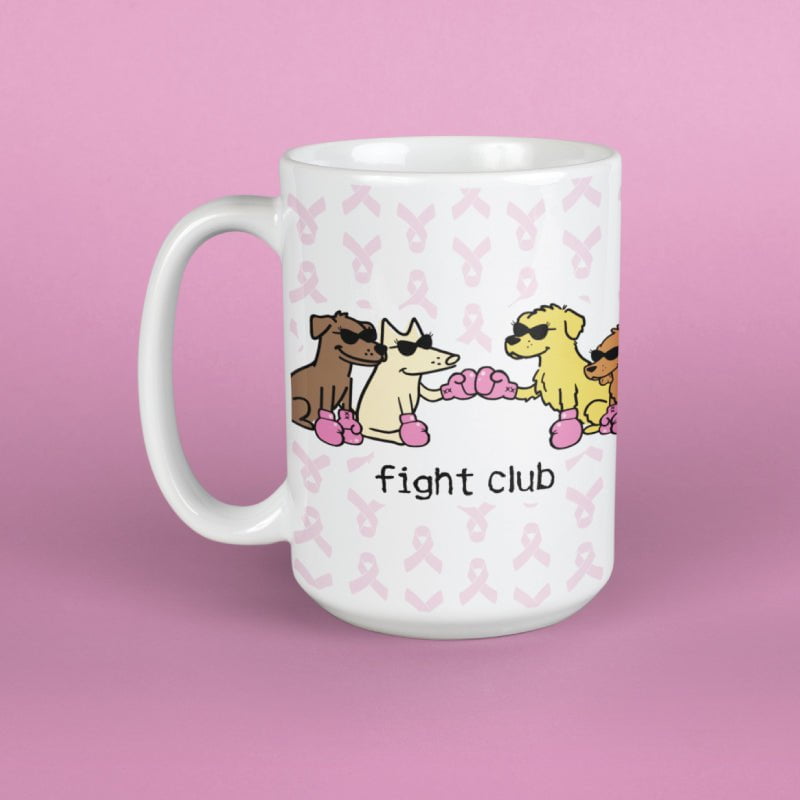 A white ceramic mug with a pink ribbon pattern and cartoon dogs wearing boxing gloves and sunglasses, with the text 'fight club' printed below. The mug is set against a solid pink background.