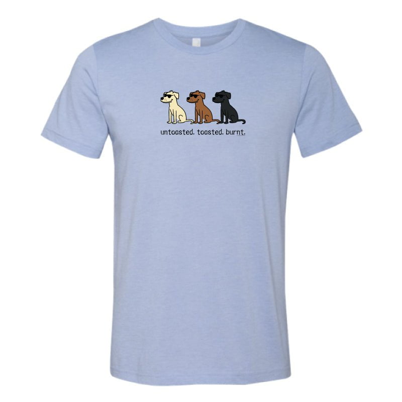 A light blue heather crewneck t-shirt featuring a graphic of three cartoon dogs in white, brown, and black, with the text 'uncoated, toasted, burnt.' printed below them.