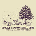 A vintage-style illustrated graphic on a warm cream background, featuring a dark purple line drawing of a tree, pumpkins, falling leaves, and a running dog. Text below reads 'SPOOKY SEASON SOCIAL CLUB' and 'SALEM, MASSACHUSETTS'.