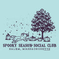 A light blue graphic print featuring a dark purple illustration of a running dog, pumpkins, a tree, and falling leaves, with the text 'SPOOKY SEASON SOCIAL CLUB' and 'SALEM, MASSACHUSETTS' below.