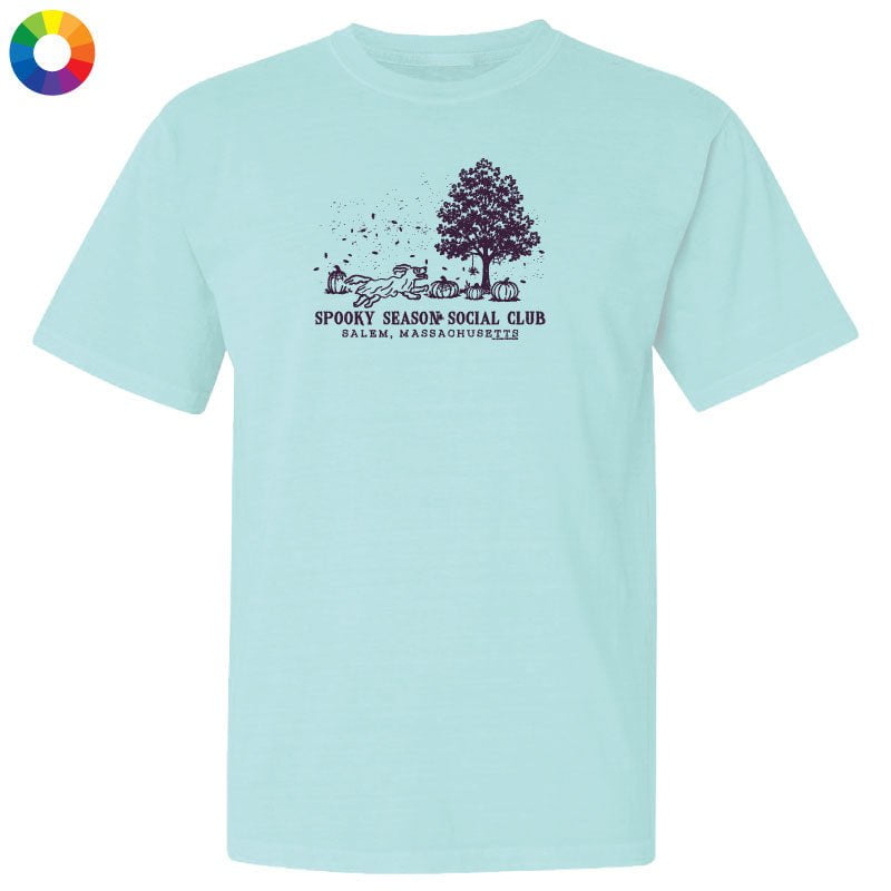 A light aqua blue short-sleeve t-shirt with a dark purple graphic on the chest depicting a tree, pumpkins, and the text 'SPOOKY SEASON SOCIAL CLUB' and 'PALM. NAPA, CA'.