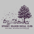 A dark purple Halloween-themed graphic on a light gray background, featuring a running dog, pumpkins, a tree, spiderwebs, and the text 'SPOOKY SEASON SOCIAL CLUB' and 'SALEM, MASSACHUSETTS'.