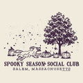 A vintage-style illustrated graphic on a warm cream background featuring a dark plum line drawing of a tree, pumpkins, falling leaves, and a running dog. Text below reads 'SPOOKY SEASON SOCIAL CLUB' and 'SALEM, MASSACHUSETTS.
